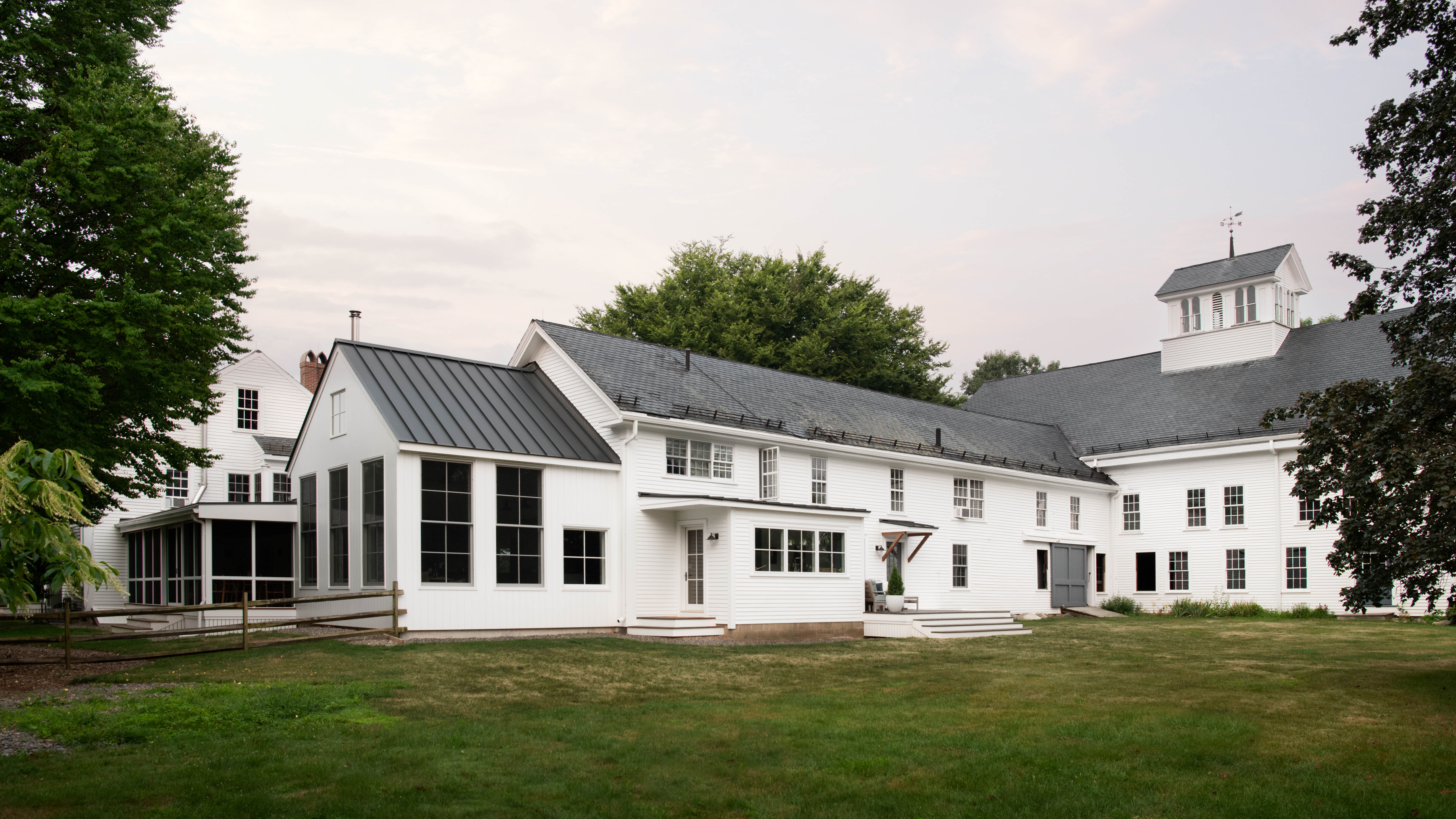 Modern white board-and-batten home addition featuring tall multi-pane sash windows and a dark standing-seam metal gable roof beside a grassy yard