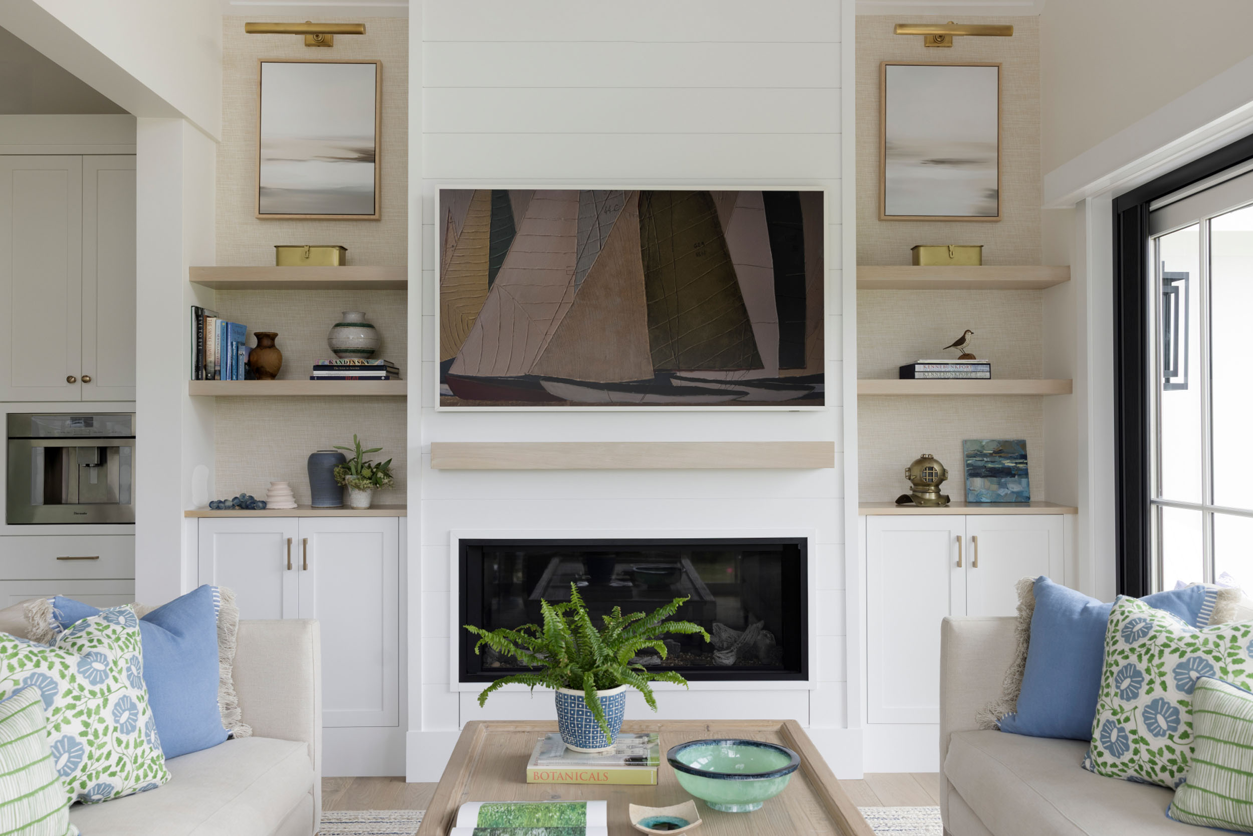 Modern living room fireplace feature with white shiplap paneling, a sleek linear fireplace, a light wood floating mantel, a Frame TV displaying sailboat artwork, and flanking built-in shelving with decorative accents.