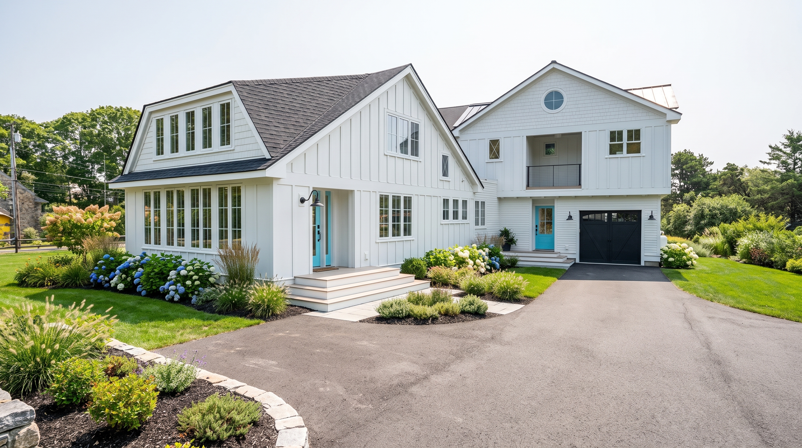 White coastal modern home featuring vertical board-and-batten siding, a dark shingle roof, a shed dormer with multiple windows, vibrant turquoise front doors, lush landscaping with flowering hydrangeas, and an asphalt driveway leading to an attached garage.
